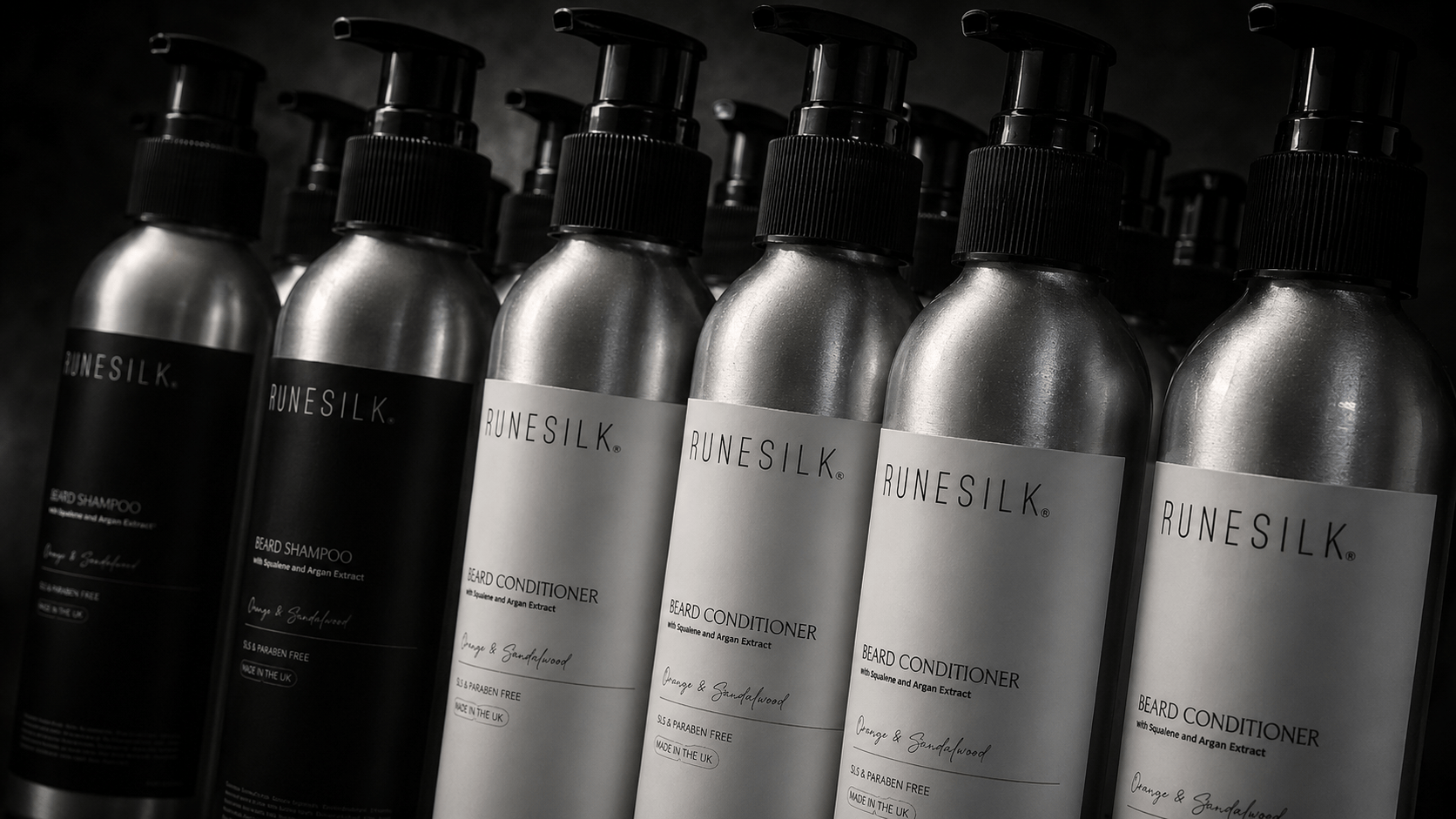 A row of RUNESILK. haircare pump bottles, including shampoo and conditioner in metallic silver and black packaging, set against a dark background.